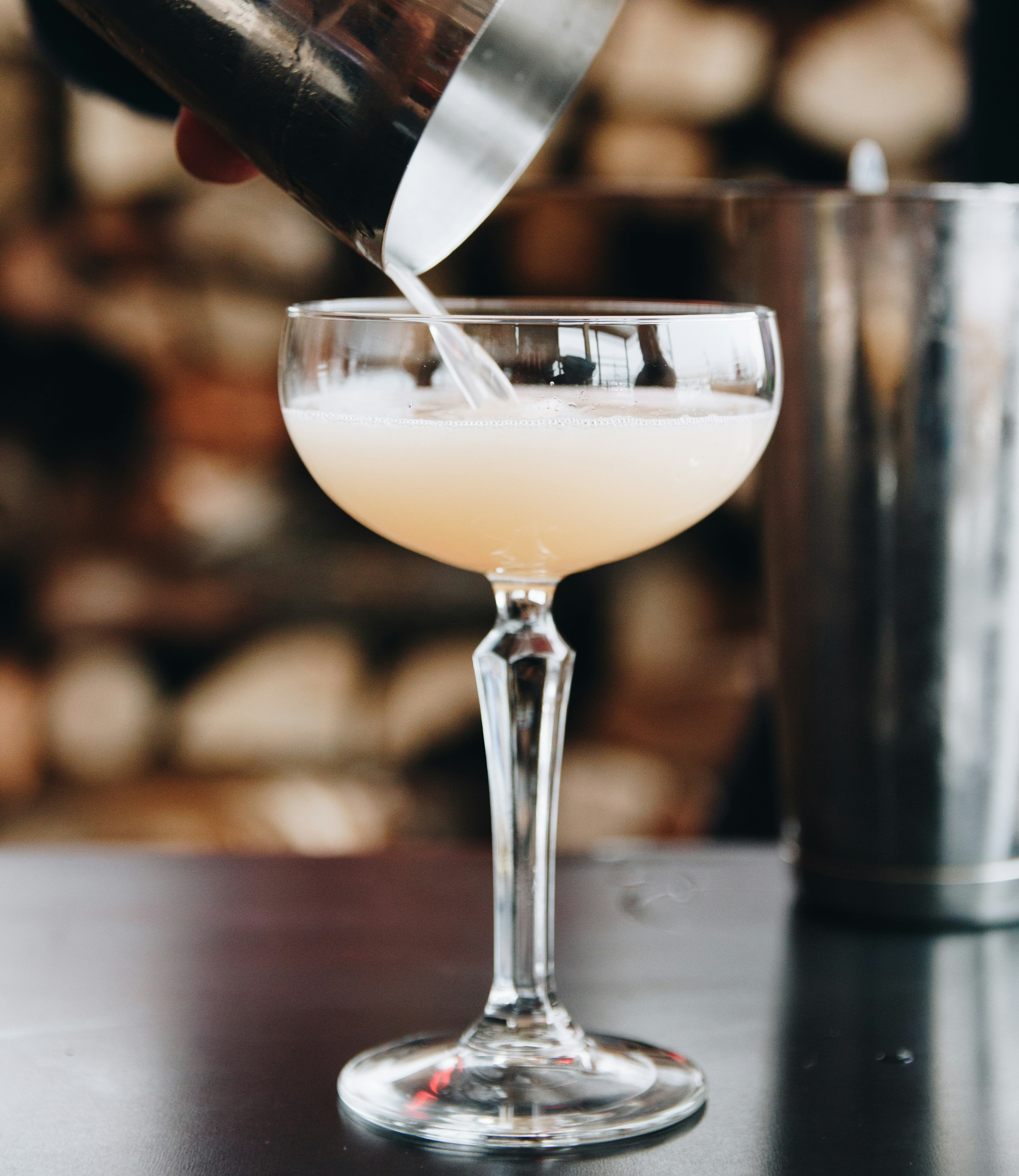 Bartender pouring a cocktail into a coupe glass